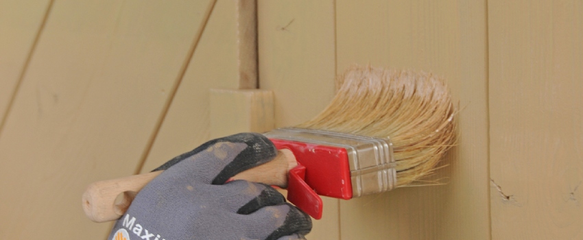 Een persoon is met een blokkwast beits aan het aanbrengen op een houten oppervlak.