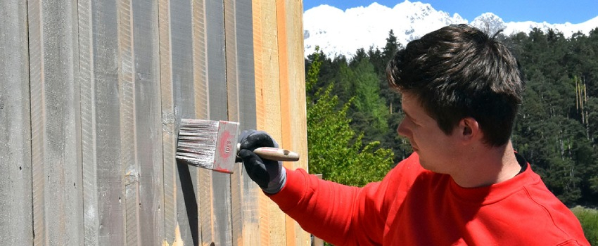 Een man is donkere beits met een blokkwast aan het aanbrengen op een houten schutting