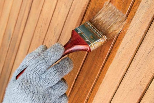 Vurenhout beits bestellen? Bekijk het uitgebreide Fixza assortiment! Persoon met handschoen aan een schutting aan het beitsen met een kwast.